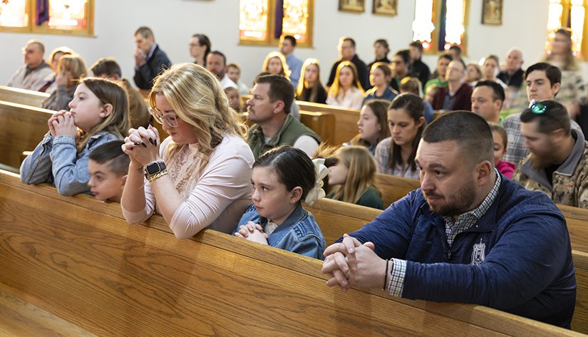 Families kneeling in prayer in the pews of a church.