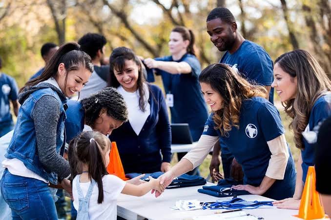 Volunteers in matching shirts greeting families at an outdoor community table.